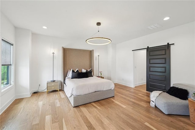 bedroom featuring light wood-type flooring, a barn door, and baseboards
