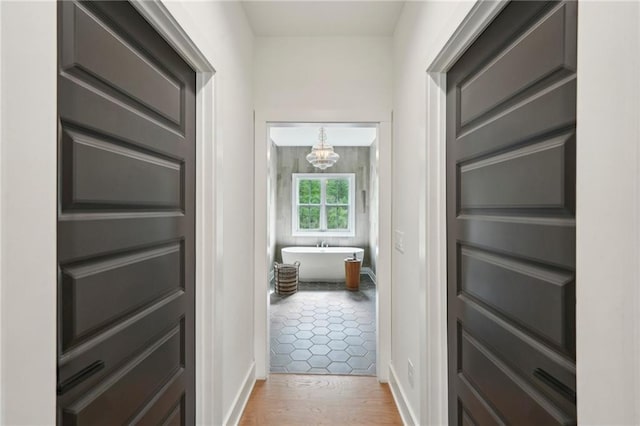 hallway featuring baseboards, an inviting chandelier, and wood finished floors