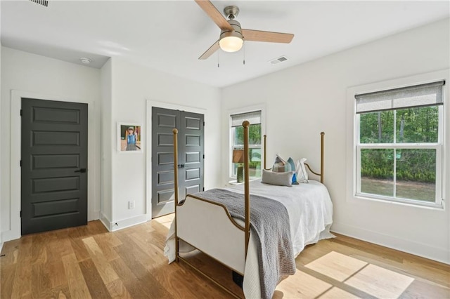 bedroom with ceiling fan, light wood finished floors, baseboards, visible vents, and a closet