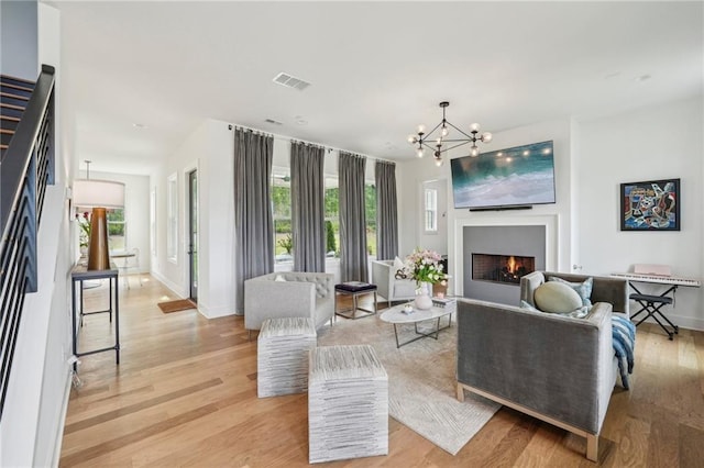 living room with visible vents, baseboards, a lit fireplace, light wood-style flooring, and a notable chandelier