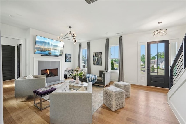 living area with a lit fireplace, baseboards, a chandelier, and light wood-style floors