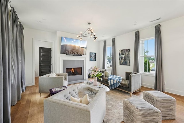 living room with a lit fireplace, visible vents, light wood-type flooring, baseboards, and an inviting chandelier