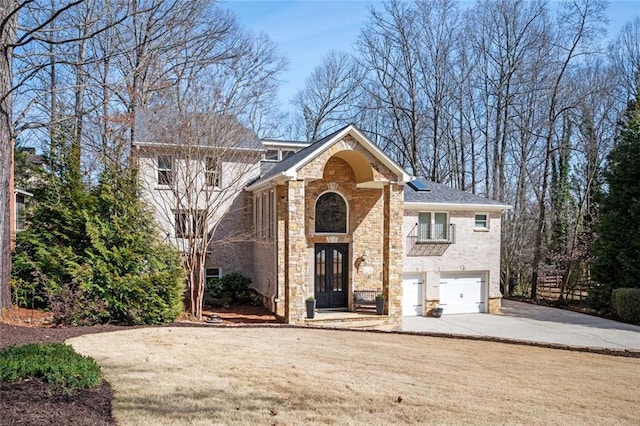 view of front of home featuring driveway, french doors, a garage, stone siding, and brick siding