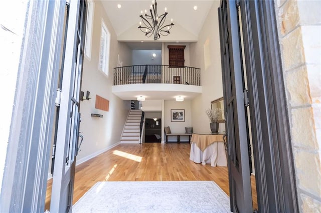 entryway with baseboards, stairs, an inviting chandelier, wood finished floors, and high vaulted ceiling