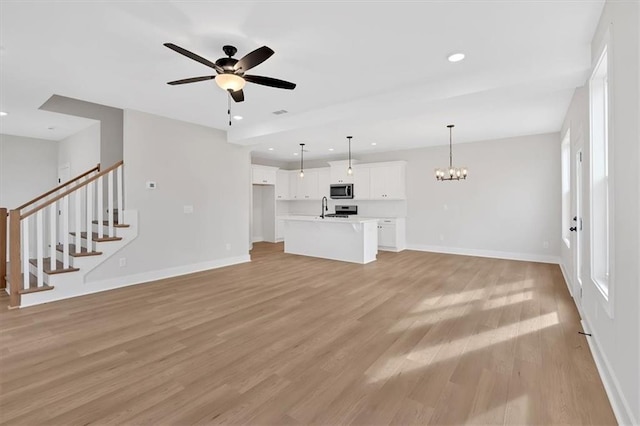 unfurnished living room featuring ceiling fan with notable chandelier, light hardwood / wood-style flooring, and sink