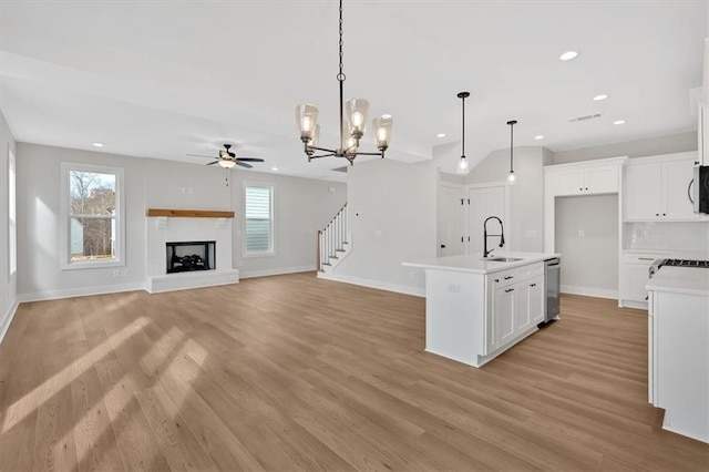 kitchen with a center island with sink, white cabinets, stainless steel dishwasher, and decorative light fixtures