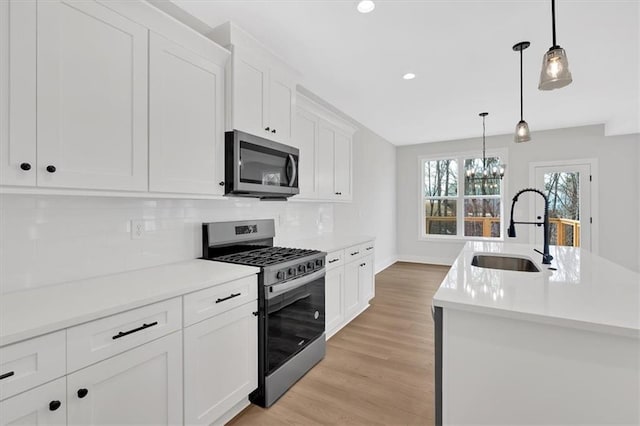 kitchen with sink, stainless steel appliances, decorative light fixtures, a kitchen island with sink, and white cabinets