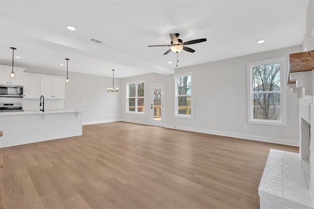 unfurnished living room with a fireplace, ceiling fan with notable chandelier, light hardwood / wood-style floors, and sink