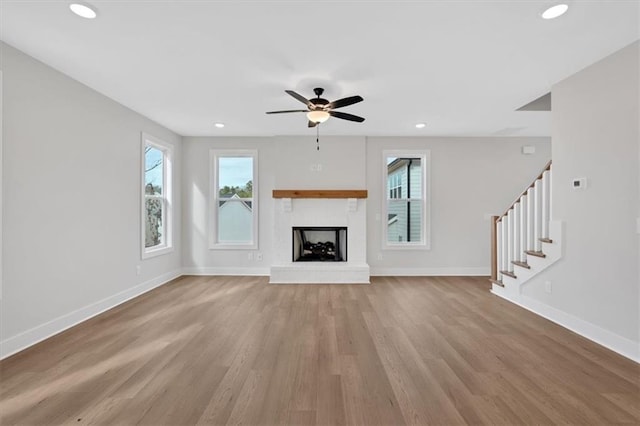 unfurnished living room with ceiling fan, a healthy amount of sunlight, light hardwood / wood-style flooring, and a brick fireplace