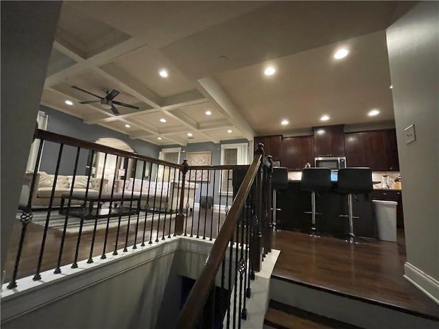 stairs with coffered ceiling, hardwood / wood-style floors, beam ceiling, and ceiling fan