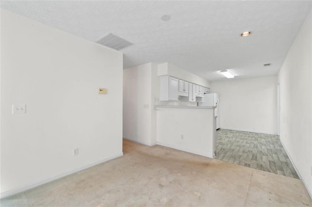 unfurnished living room featuring baseboards, visible vents, a textured ceiling, and light colored carpet