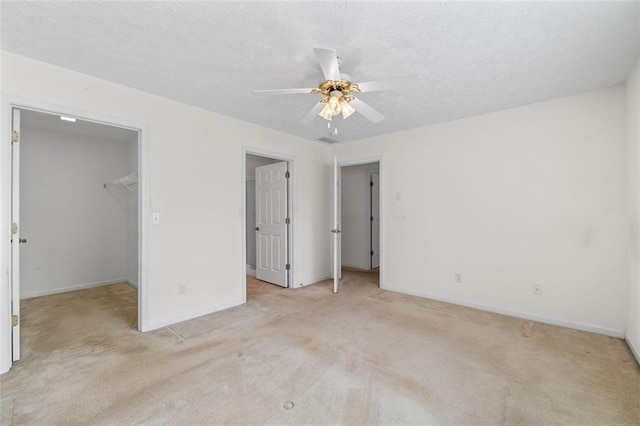 unfurnished bedroom featuring a walk in closet, light colored carpet, a ceiling fan, a textured ceiling, and baseboards