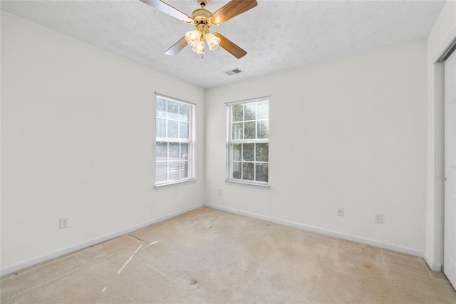 empty room featuring visible vents, light carpet, ceiling fan, a textured ceiling, and baseboards