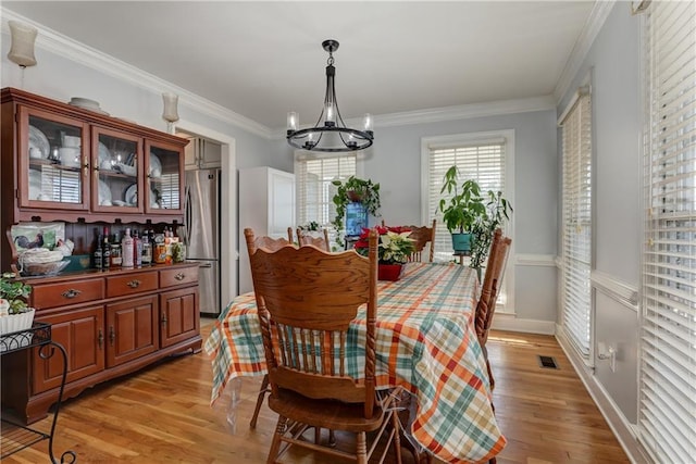 dining area with a notable chandelier, light hardwood / wood-style floors, and crown molding