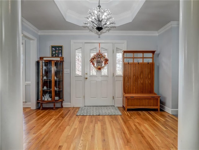 foyer featuring a chandelier, light wood-style flooring, crown molding, a tray ceiling, and baseboards