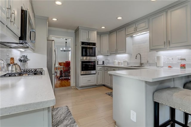 kitchen with gray cabinets, appliances with stainless steel finishes, a peninsula, a sink, and ornamental molding