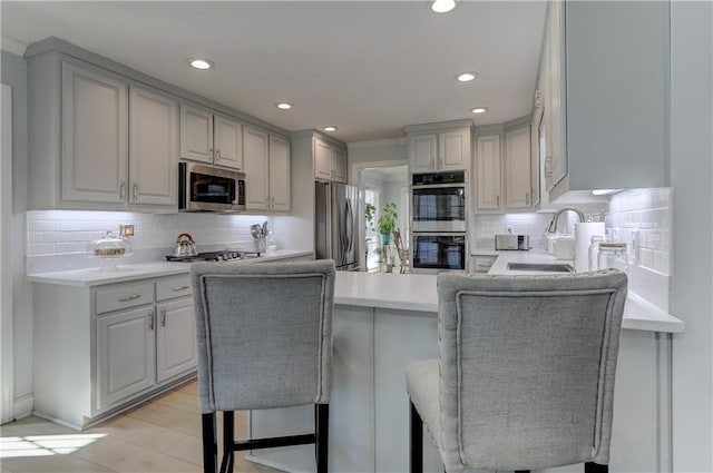 kitchen featuring appliances with stainless steel finishes, a sink, decorative backsplash, light countertops, and a peninsula