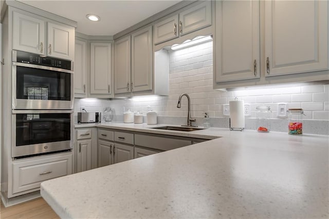 kitchen with a sink, stainless steel double oven, gray cabinets, light countertops, and recessed lighting