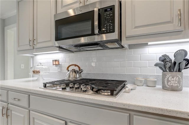 kitchen with stainless steel appliances, backsplash, white cabinets, and light stone countertops