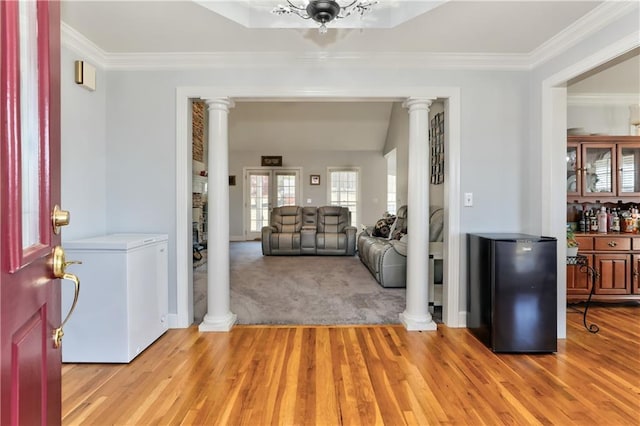 entrance foyer with ornate columns, light wood-style flooring, ornamental molding, baseboards, and light carpet