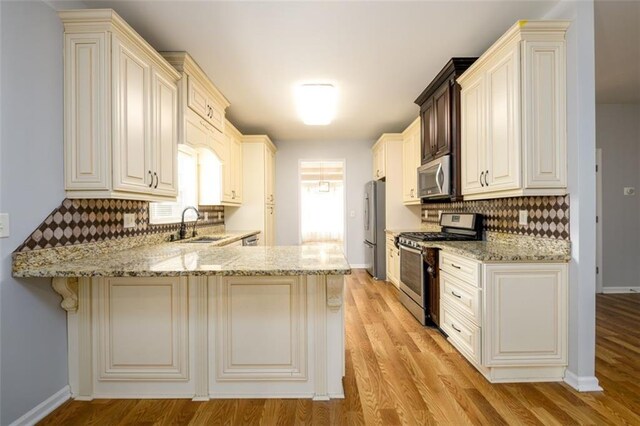 kitchen with light stone counters, stainless steel appliances, kitchen peninsula, and light hardwood / wood-style flooring