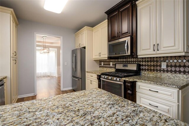 kitchen featuring light stone countertops, stainless steel appliances, light wood-type flooring, and decorative backsplash