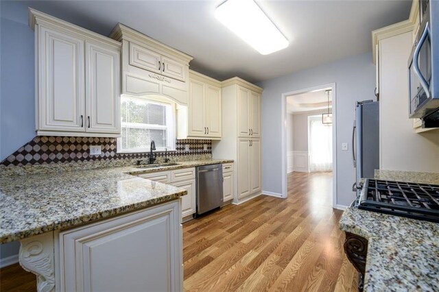 kitchen with light stone counters, appliances with stainless steel finishes, backsplash, and light hardwood / wood-style flooring