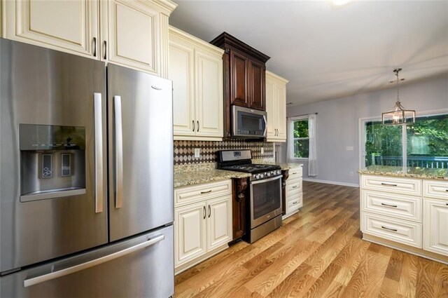 kitchen featuring pendant lighting, decorative backsplash, light hardwood / wood-style flooring, appliances with stainless steel finishes, and light stone countertops