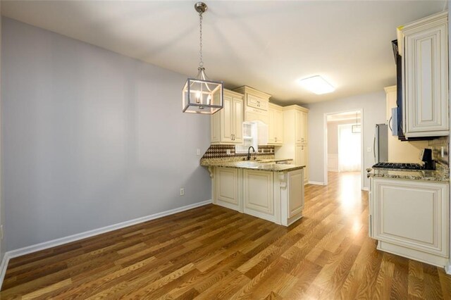 kitchen with backsplash, light stone countertops, pendant lighting, light wood-type flooring, and sink