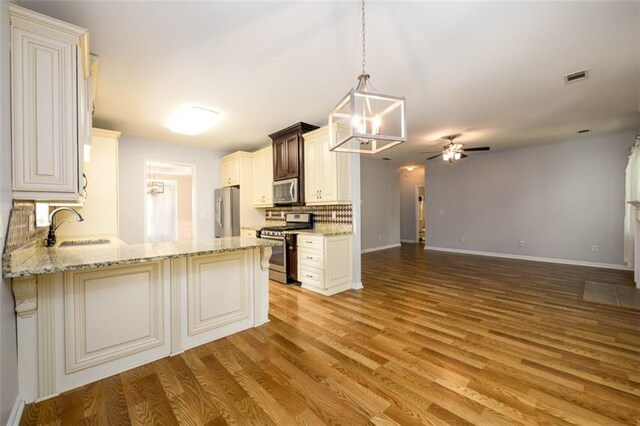 kitchen featuring light wood-type flooring, sink, decorative light fixtures, stainless steel appliances, and ceiling fan with notable chandelier