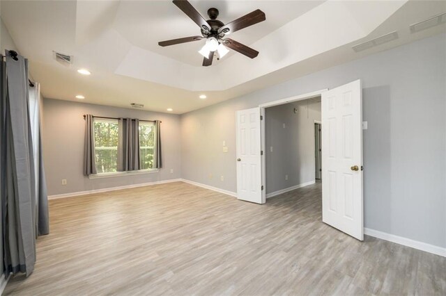 empty room featuring ceiling fan, a tray ceiling, and light hardwood / wood-style floors