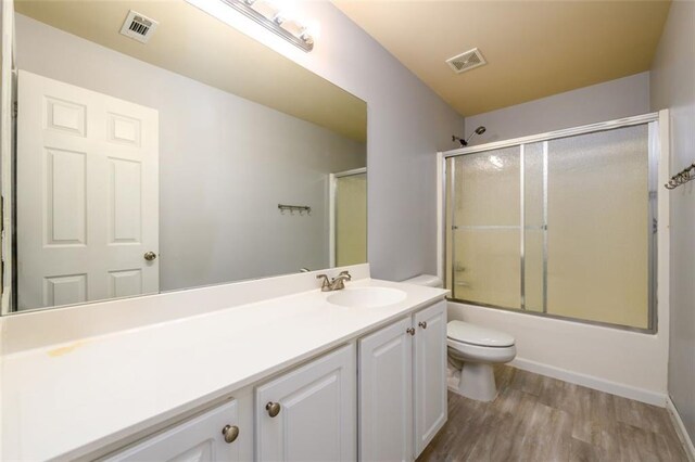 full bathroom featuring bath / shower combo with glass door, hardwood / wood-style flooring, vanity, and toilet