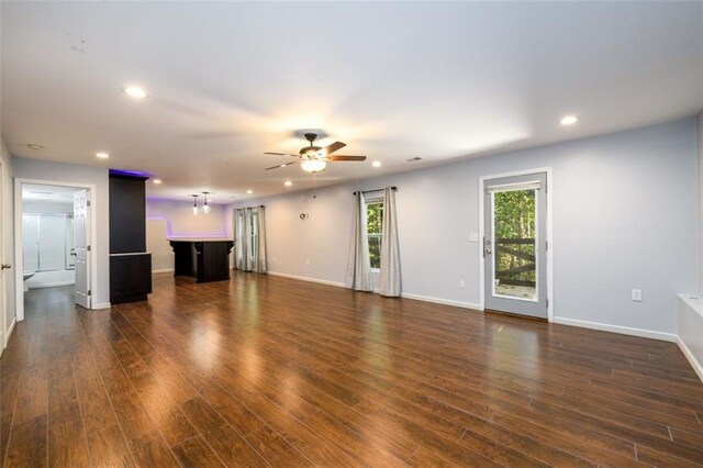 unfurnished living room with bar area, dark hardwood / wood-style flooring, and ceiling fan