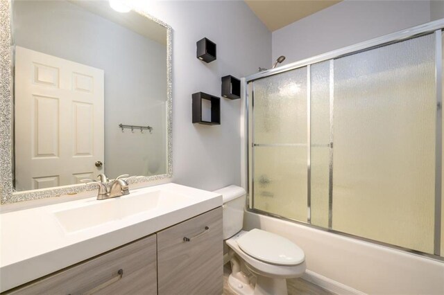 full bathroom with combined bath / shower with glass door, vanity, and toilet