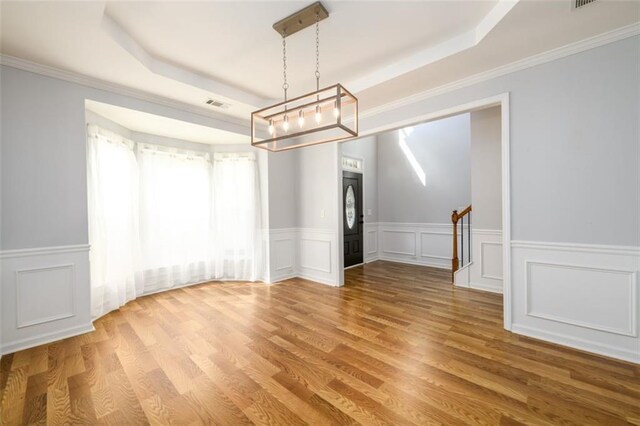 unfurnished dining area with ornamental molding, a raised ceiling, and hardwood / wood-style flooring