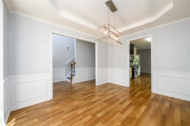 unfurnished dining area featuring ornamental molding, a tray ceiling, and hardwood / wood-style flooring