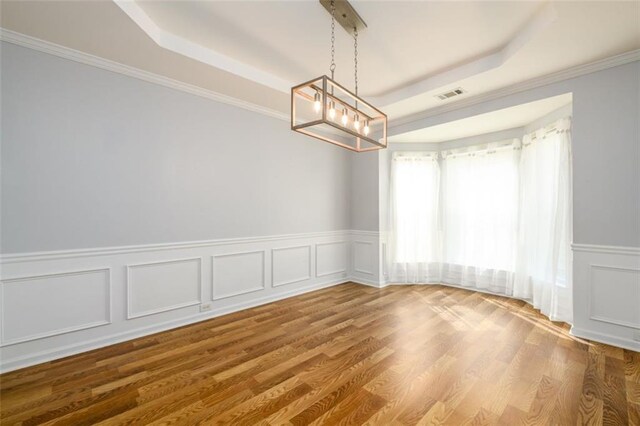 unfurnished room featuring a raised ceiling, ornamental molding, and hardwood / wood-style flooring