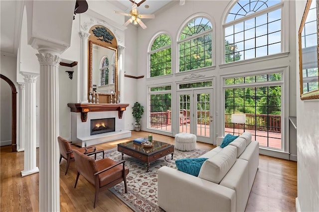 11569 Finley St, Suwanee, GA 30024 - living room featuring decorative columns, a towering ceiling, a ceiling fan, a warm lit fireplace, and wood finished floors