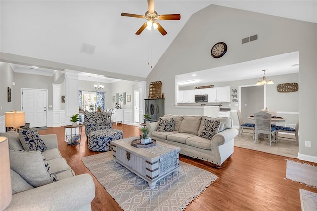 living area featuring ceiling fan with notable chandelier, decorative columns, wood finished floors, and visible vents