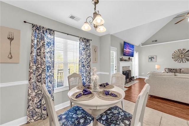 tiled dining area with vaulted ceiling, a fireplace with flush hearth, baseboards, and visible vents