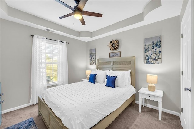 carpeted bedroom featuring a tray ceiling, visible vents, baseboards, and ceiling fan