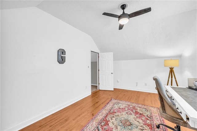 office area featuring light wood-style flooring, a textured ceiling, baseboards, ceiling fan, and vaulted ceiling