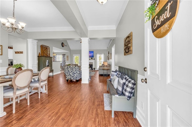 foyer featuring lofted ceiling, light wood-style flooring, decorative columns, ornamental molding, and a notable chandelier