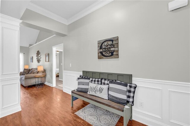 sitting room with crown molding, a decorative wall, wood finished floors, and a wainscoted wall