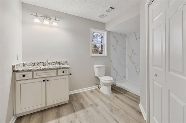 bathroom with vanity, wood-type flooring, a shower, a textured ceiling, and toilet