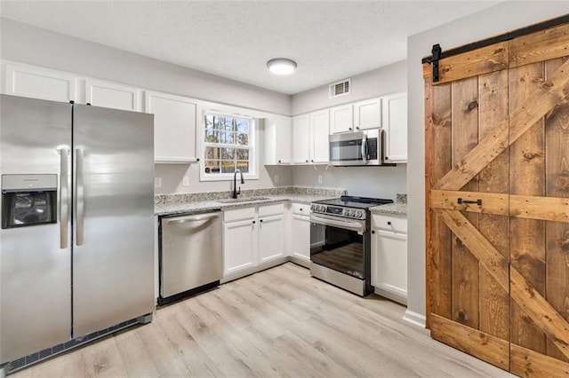 kitchen featuring sink, light stone counters, appliances with stainless steel finishes, a barn door, and white cabinets