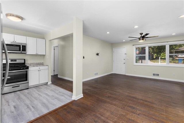 kitchen featuring stainless steel appliances, open floor plan, white cabinets, wood finished floors, and baseboards