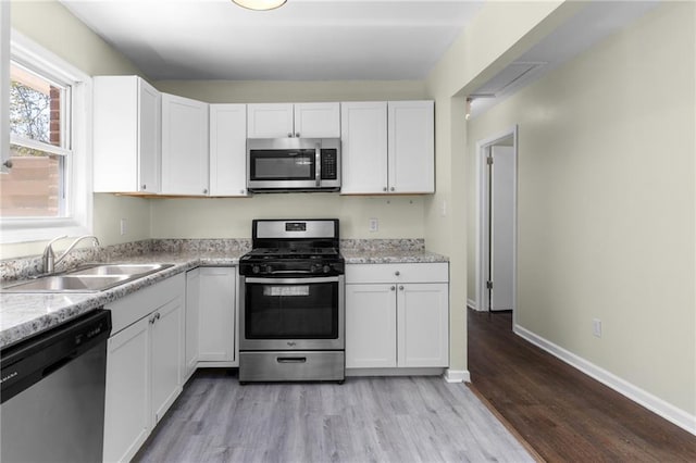 kitchen featuring appliances with stainless steel finishes, light wood-type flooring, a sink, and white cabinetry