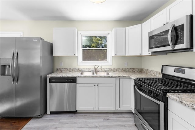 kitchen featuring light wood finished floors, appliances with stainless steel finishes, a sink, and white cabinetry