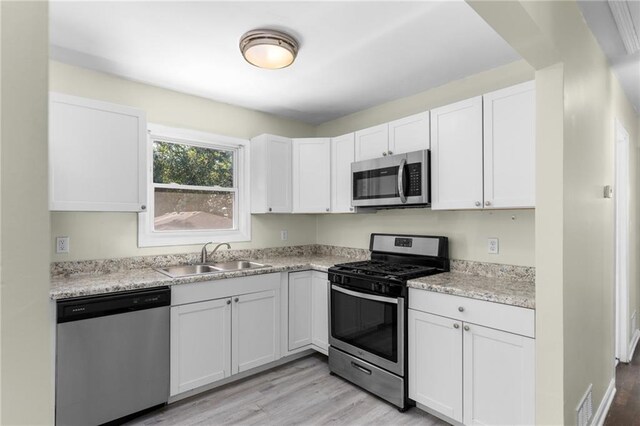 kitchen featuring stainless steel appliances, visible vents, white cabinets, a sink, and light wood-type flooring